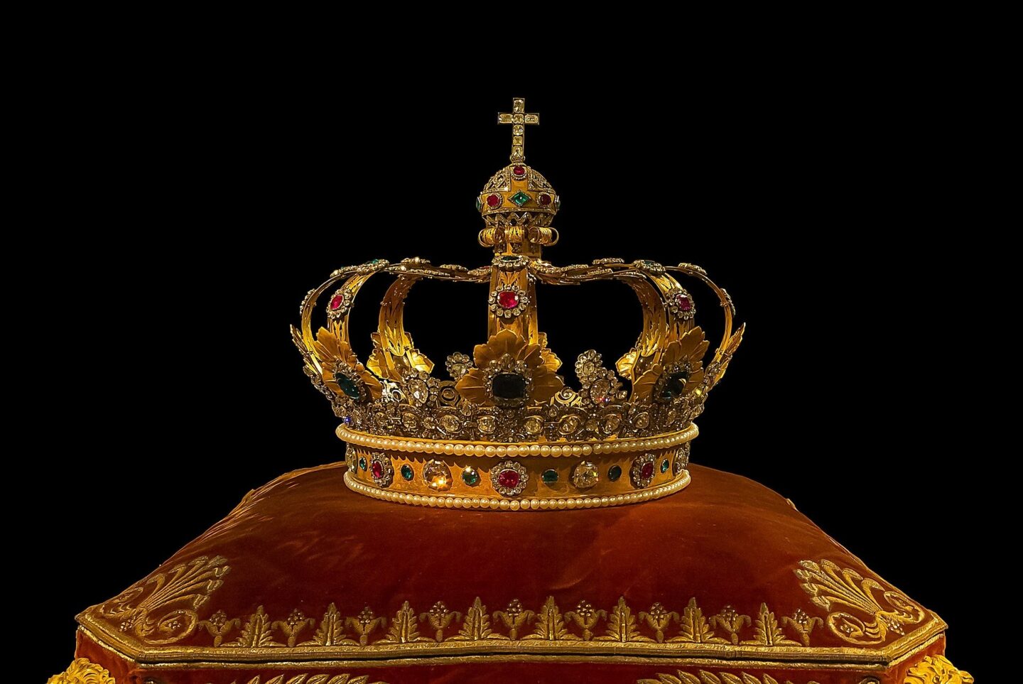 Gold jeweled crown sitting on a red pillow